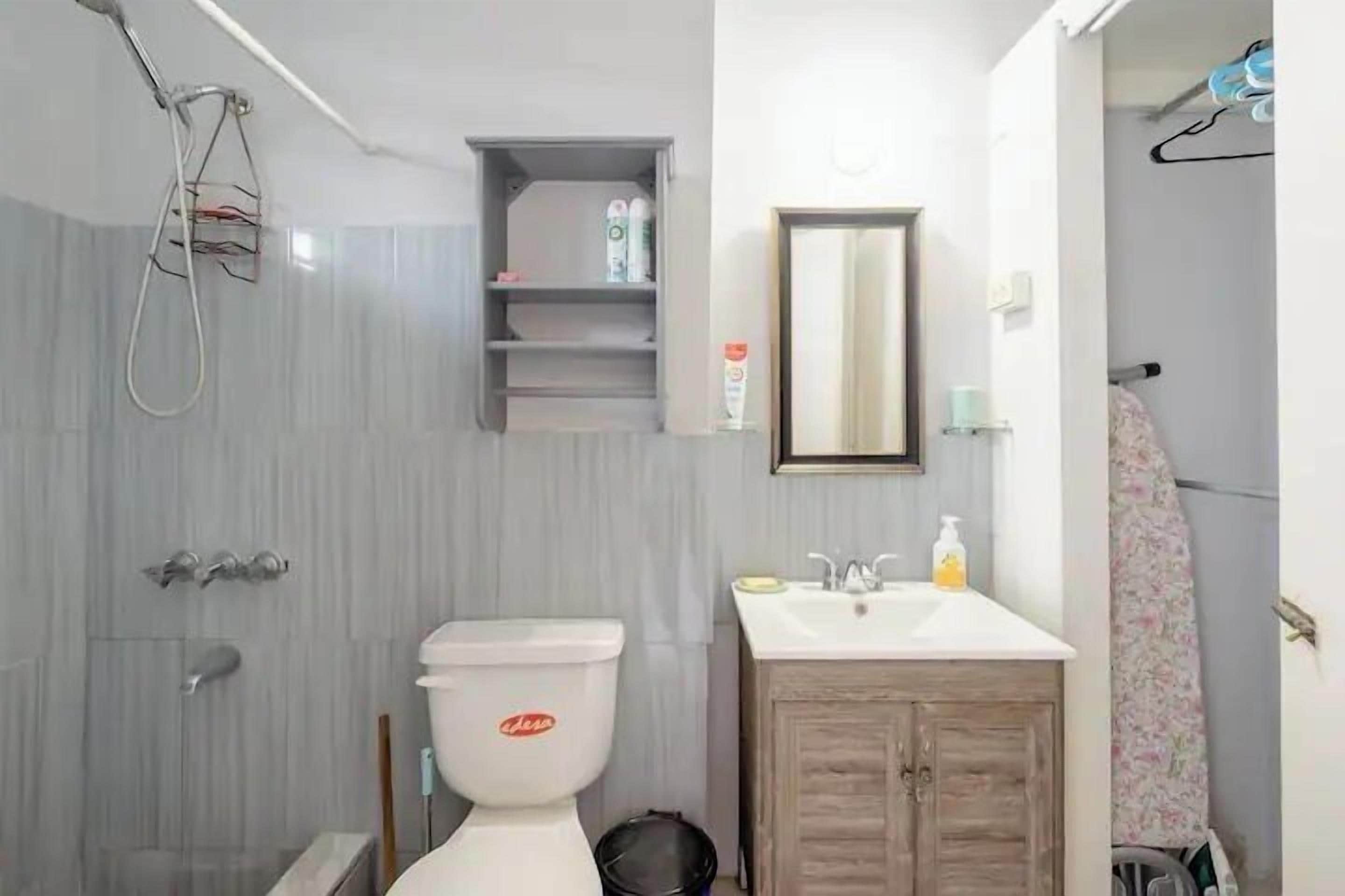 A bathroom with a toilet, sink, and shower. There is a shelf with toiletries and a mirror above the sink.