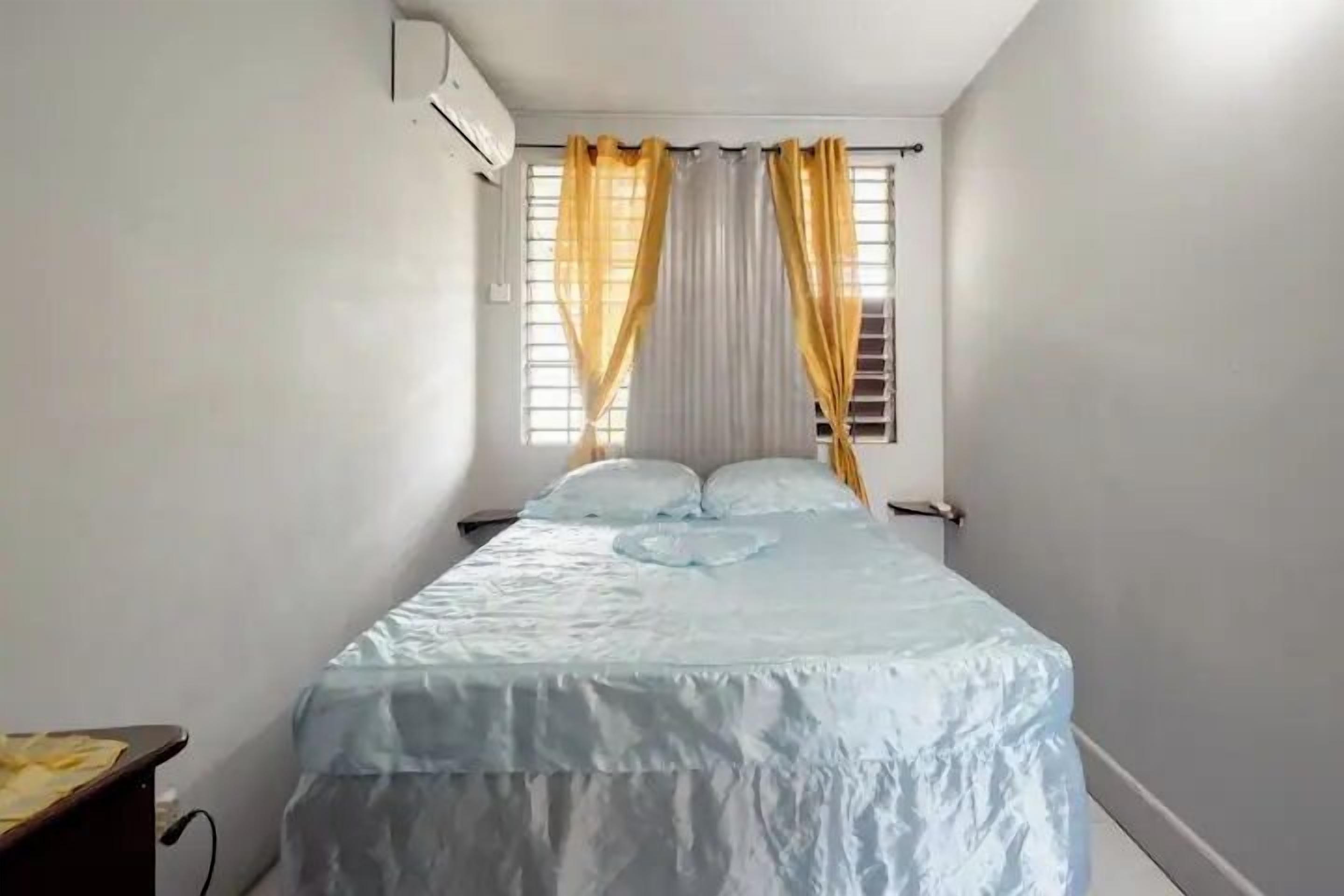 A bedroom with a bed, curtains, and an air conditioning unit.