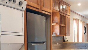 Una cocina con armarios de madera, un refrigerador de acero inoxidable, un horno blanco y un cubo de basura azul.