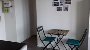 Ein Zimmer mit einem Holztisch und zwei Stühlen, einer weißen Wand mit mehreren gerahmten Bildern und einer Tür zu einem anderen Raum.