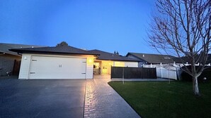 Una casa residencial con garaje, entrada pavimentada, patio cercado y un árbol.