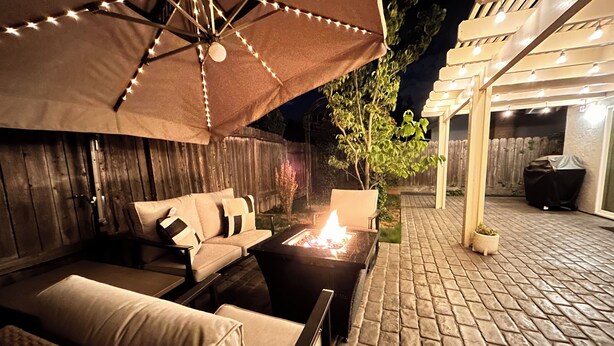 Un patio al aire libre con una chimenea, zona de estar y luces colgantes.