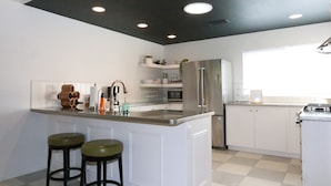 Una cocina moderna con armarios blancos, un refrigerador de acero inoxidable, una isla integrada con taburetes e iluminación empotrada en el techo.
