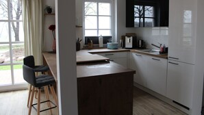 Moderni keittiö, jossa on suuri ikkuna, puiset baarituolit ja valkoiset kaapit.