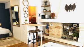 Un salon moderne avec un plancher en bois, un canapé blanc, une table à manger et un coin cuisine doté d’un mur en briques et d’une cheminée.