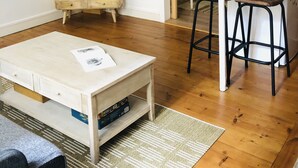 Un espace de vie compact comprenant un téléviseur, une table en bois, des tabourets de bar et un coin cuisine visible à travers une porte ouverte.