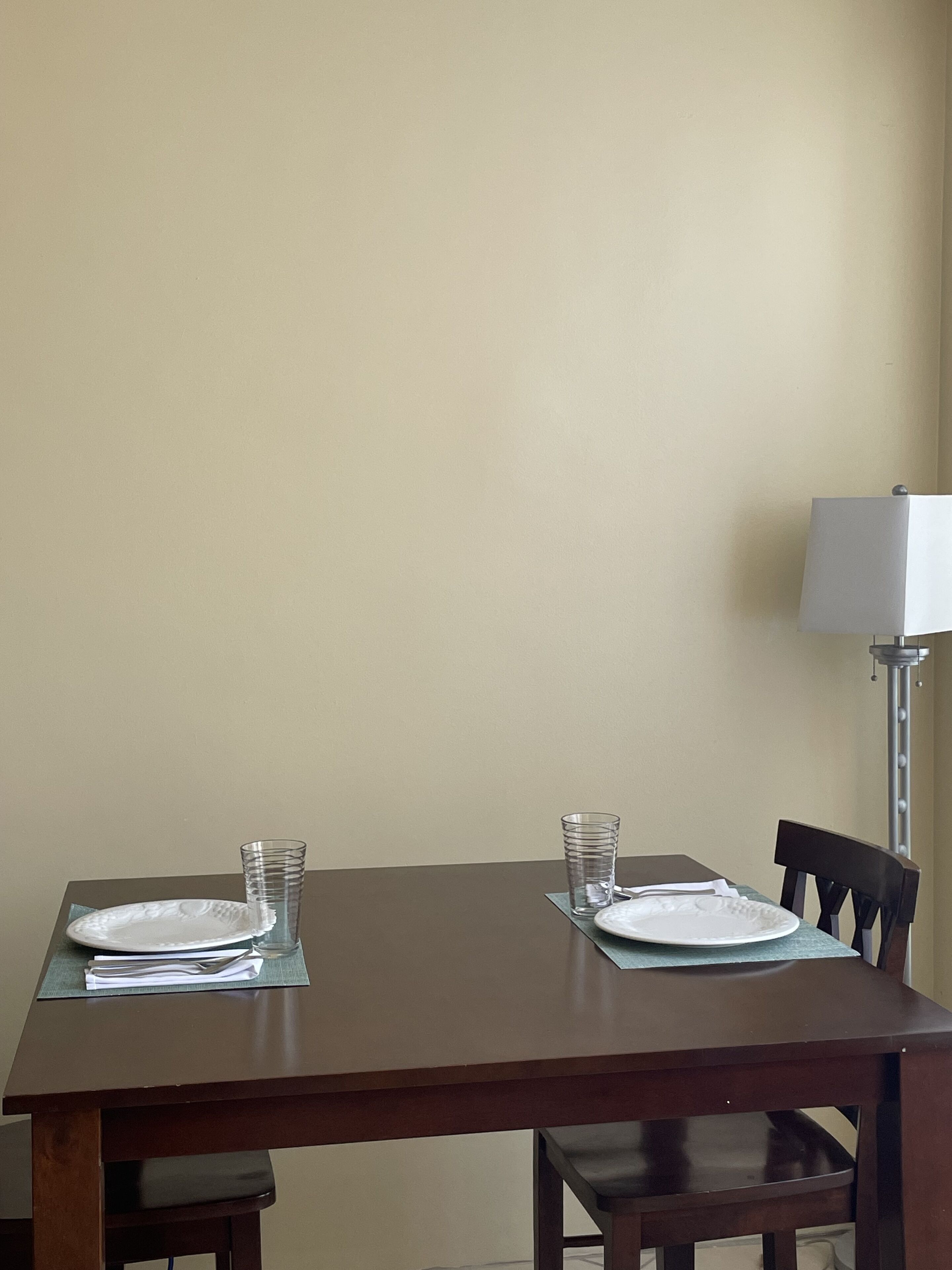 A dining table with two plates and two glasses, a lamp, and a chair.