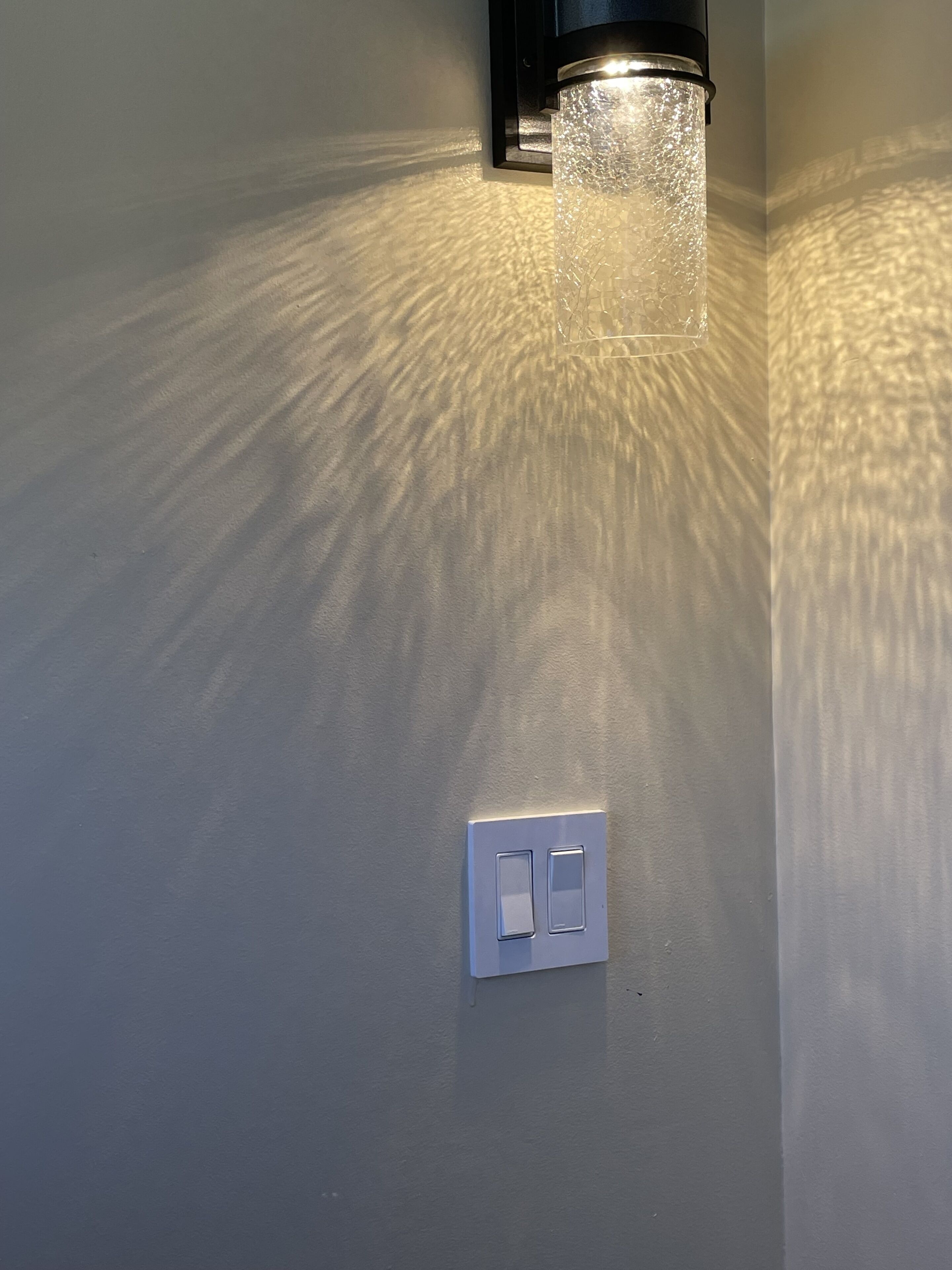 A wall-mounted light fixture with a textured glass cover and a switch below it.