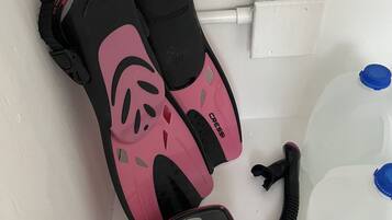Een witte plank met een set duikuitrusting in roze en zwart, inclusief vinnetjes, snorkel en masker. Rechts staan twee blauwe waterflessen.