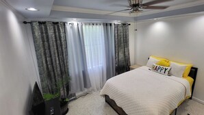 Un dormitorio con cama, cortinas, ventilador de techo y una planta pequeña.