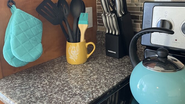 Una encimera de cocina con una tetera, una taza con utensilios y un juego de cuchillos.