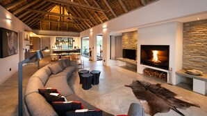 A modern living room with a curved gray sofa, a stone fireplace, and a large leather rug.