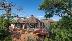 A thatched-roof bungalow with a wooden deck, surrounded by dense greenery.