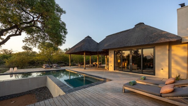 A modern villa with a pool, outdoor seating, and thatched-roof structures.