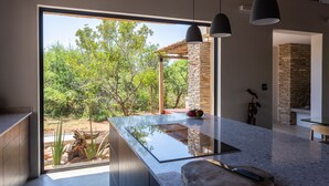 A modern kitchen with a large island, a stone accent wall, and a view of a lush garden.