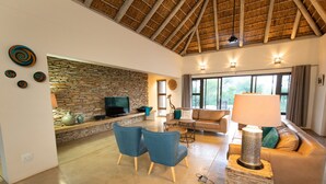 A spacious living area with a stone wall, a large window, a sofa, and a coffee table. - Villa Bushman: Wonderful luxury and attractive villa (Hoedspruit)