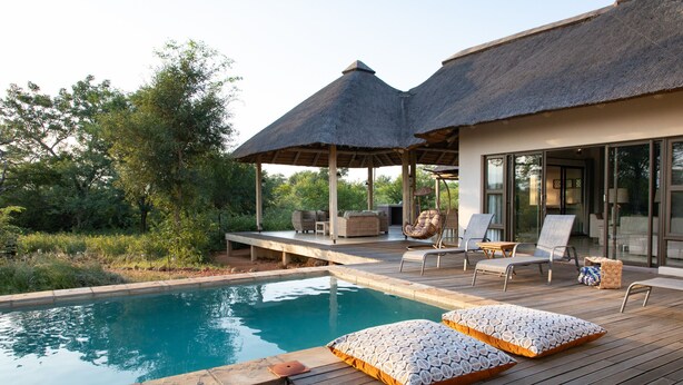 A poolside area with a wooden deck, lounge chairs, and a covered seating area with a thatched roof. - Villa Bushman: Wonderful luxury and attractive villa (Hoedspruit)