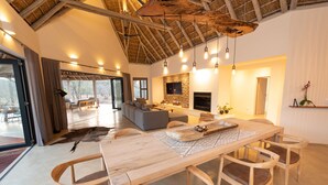 A spacious living area with a large wooden dining table, comfortable seating, a fireplace, and a television mounted on the wall. - Villa Appelblaar: luxury 4 bedroom villa home in the South African bush (Hoedspruit)