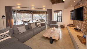 A modern living room with a sectional sofa, a coffee table, and a stone accent wall. - Villa Appelblaar: luxury 4 bedroom villa home in the South African bush (Hoedspruit)