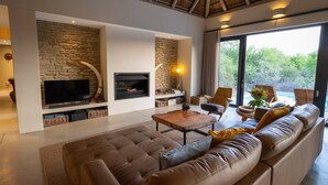 A modern living room with a stone wall, a fireplace, a flat-screen TV, and a large window overlooking greenery.