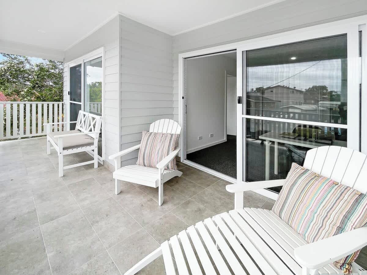 A balcony with white chairs and a glass door leading to a patio area.