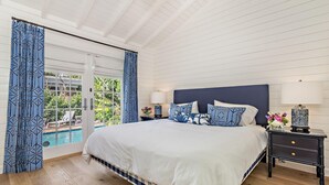 Un dormitorio con una cama grande, una mesita de noche, una lámpara y vista a una piscina a través de un ventanal.