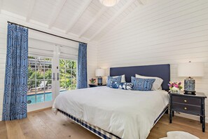 Camera da letto con un letto grande, un comodino, una lampada e vista su una piscina attraverso una porta in vetro.