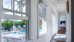 Un pasillo luminoso con ventanas amplias, vista a la piscina y una cama al fondo.