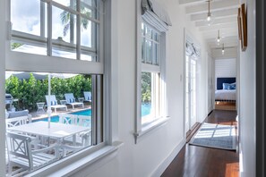 Un corridoio luminoso con ampie finestre, vista piscina e un letto in lontananza.