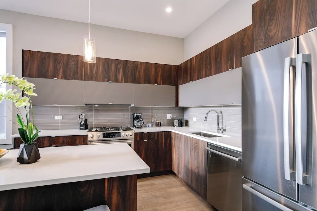 Une cuisine moderne avec des meubles en bois foncé, des appareils électroménagers en acier inoxydable et un plan de travail blanc.