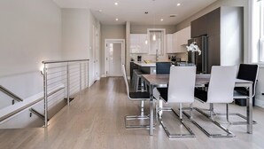 Een moderne keuken met roestvrijstalen apparatuur, een eethoek met een houten tafel en witte stoelen, en een trap met metalen leuningen.