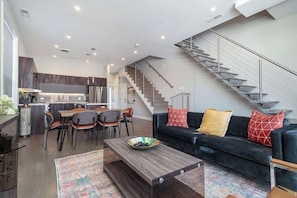 A modern living room with a dark-colored sofa, a coffee table, and a staircase leading to an upper level. - 2 Newly Built Luxury Condos with Private Roofdeck! (Chicago)