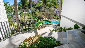 A balcony with a stone floor, surrounded by tropical plants and a pool in the background. - Tranquility at La Isla Brisas 2 (Sayulita)