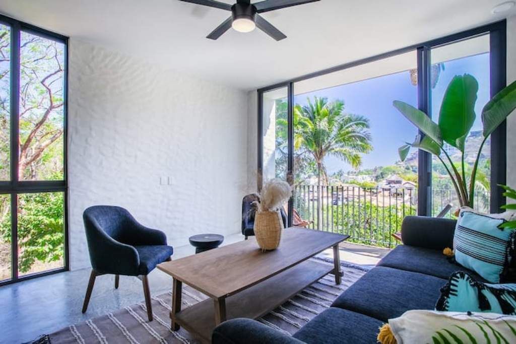 A modern room with large windows, a ceiling fan, a sofa, a coffee table, and a chair.