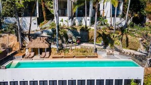 Ein modernes Hotel mit Schwimmbad, Palmen und einem Gebäude mit Strohdach.