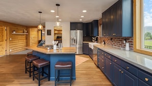 Een moderne keuken met houten wanden, een centraal eiland met krukken, roestvrijstalen apparatuur en een groot raam met uitzicht.