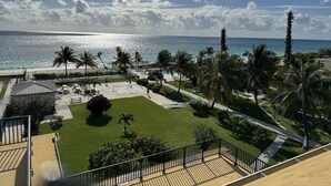 A view of a beachside property with a tennis court, palm trees, and a pool.