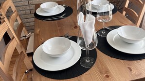 A wooden dining table set with white plates, black placemats, and a vase with dried flowers.