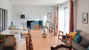 A dining area with a wooden table and chairs, a sofa, and a potted plant. - 靠近巴黎戴高乐机场，国际展览中心，法国体育场，迪斯尼乐园，花园365平面，200平面别墅，可容纳14个人，五间卧室，三个浴室，花园可烤肉，大餐桌和阳伞，三个秋千 (Aulnay-sous-Bois)