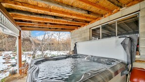 Un bain à remous sous une pergola en bois, avec vue sur un paysage enneigé.