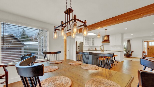 Un vaste espace dédié à la salle à manger, avec une table et des chaises en bois, un lustre et une vue sur l’extérieur grâce à de grandes fenêtres.