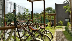A bicycle parking area with a pergola overhead, a stone pathway, and a fenced garden area. - Apartamento 02 Quartos - São Miguel dos Milagres (São Miguel dos Milagres)