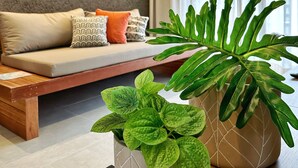 A modern living room with a sofa, decorative wall art, and potted plants. - Apartamento 02 Quartos - São Miguel dos Milagres (São Miguel dos Milagres)