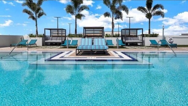 A swimming pool with lounge chairs and palm trees. - Stylish 2BR Condo. Walk to Restaurants & Shops (Doral)