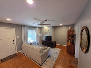 A living room with a sofa, TV, ceiling fan, and wooden flooring. - Cozy Home in the heart of San Antonio. (San Antonio)