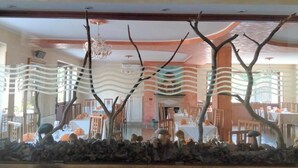 Un restaurante con una decoración moderna, que presenta un área central de comedor con mesas y sillas, y una escultura decorativa de un árbol en primer plano.