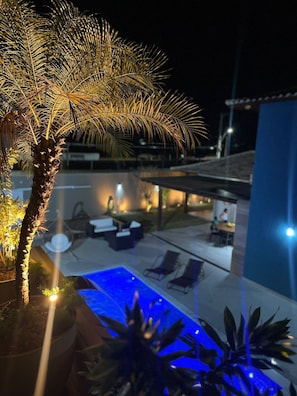 A pool area with lounge chairs, a palm tree, and a building in the background.