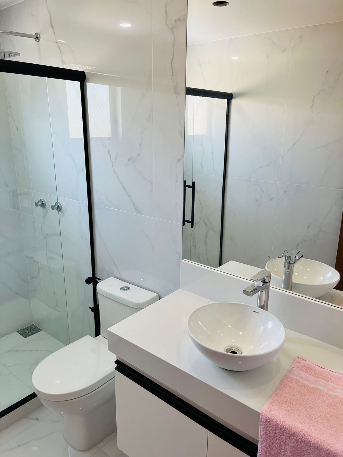Ein modernes Badezimmer mit einer gläsernen Duschkabine, einer weißen Toilette, einem weißen Waschbecken mit Schüssel und einem großen Spiegel.
