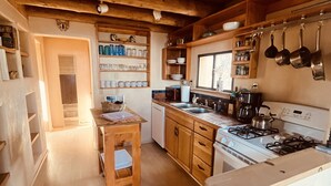 A kitchen with wooden cabinets, a stove, and hanging pots. - Taos Mountain Views Cozy Home Special Rates (El Prado)