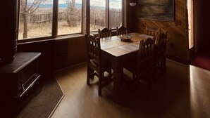 A dining area with a wooden table and chairs, large windows with a view of the outdoors, and a ceiling fan. - Taos Mountain Views Cozy Home Special Rates (El Prado)